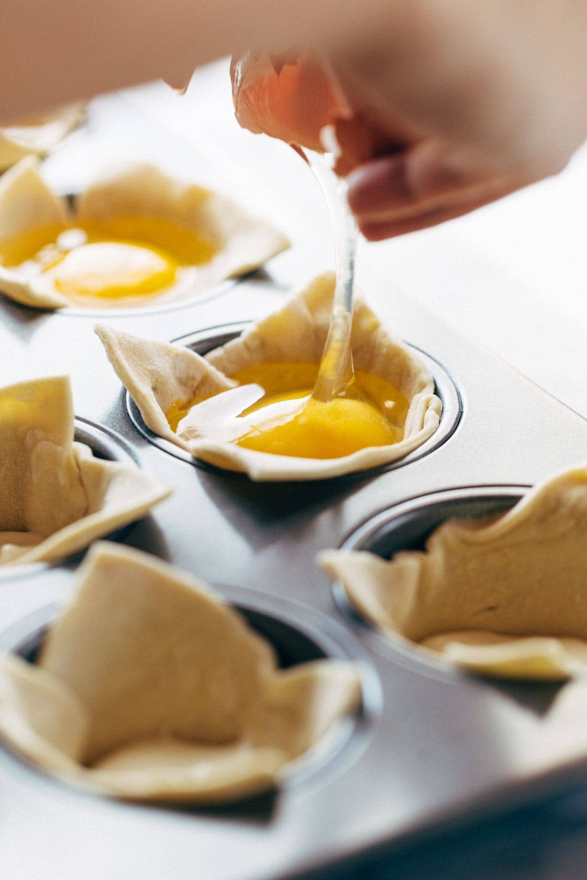 Cracking eggs into puff pastry in muffin tin.