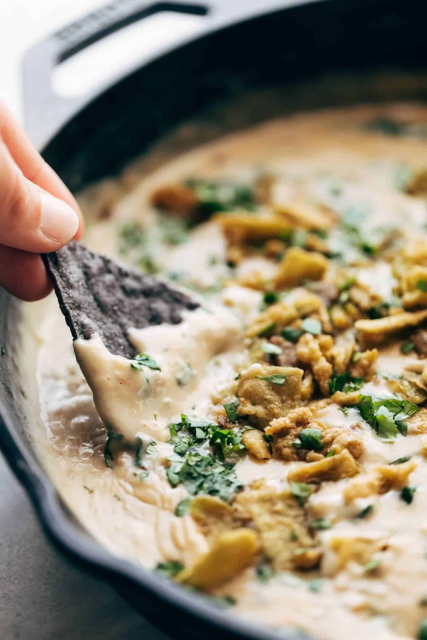Spinach Queso is SO GOOD. Simple, real food, no processed cheese! Perfect for parties and get-togethers. | pinchofyum.com Tortilla chip dipping into Spinach Queso