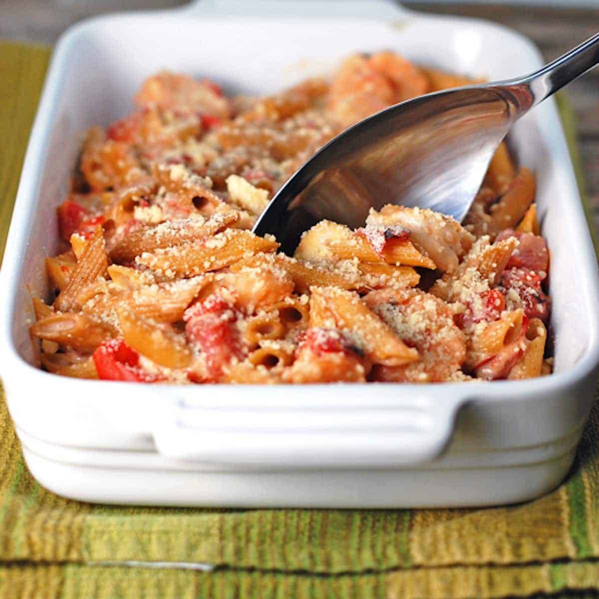 Garlic shrimp baked penne with a spoon in a white baking dish on a green napkin.
