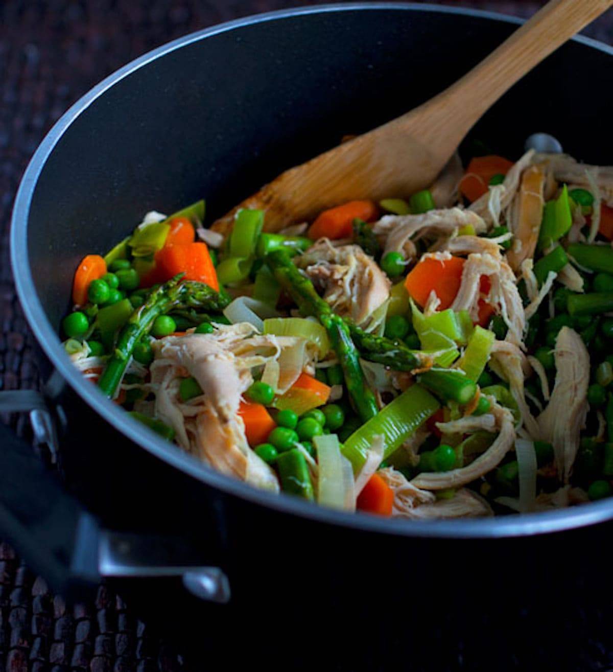 Garlic chicken and vegetable pot pie in a pan with a wooden spoon.